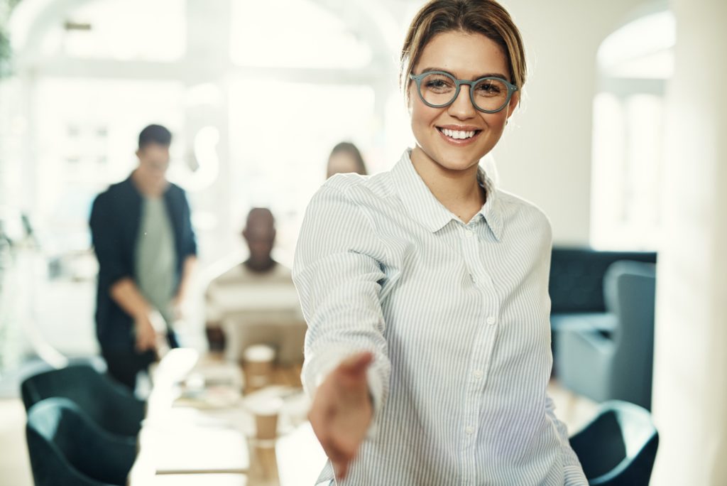 Friendly young businesswoman standing in an office extending a handshake